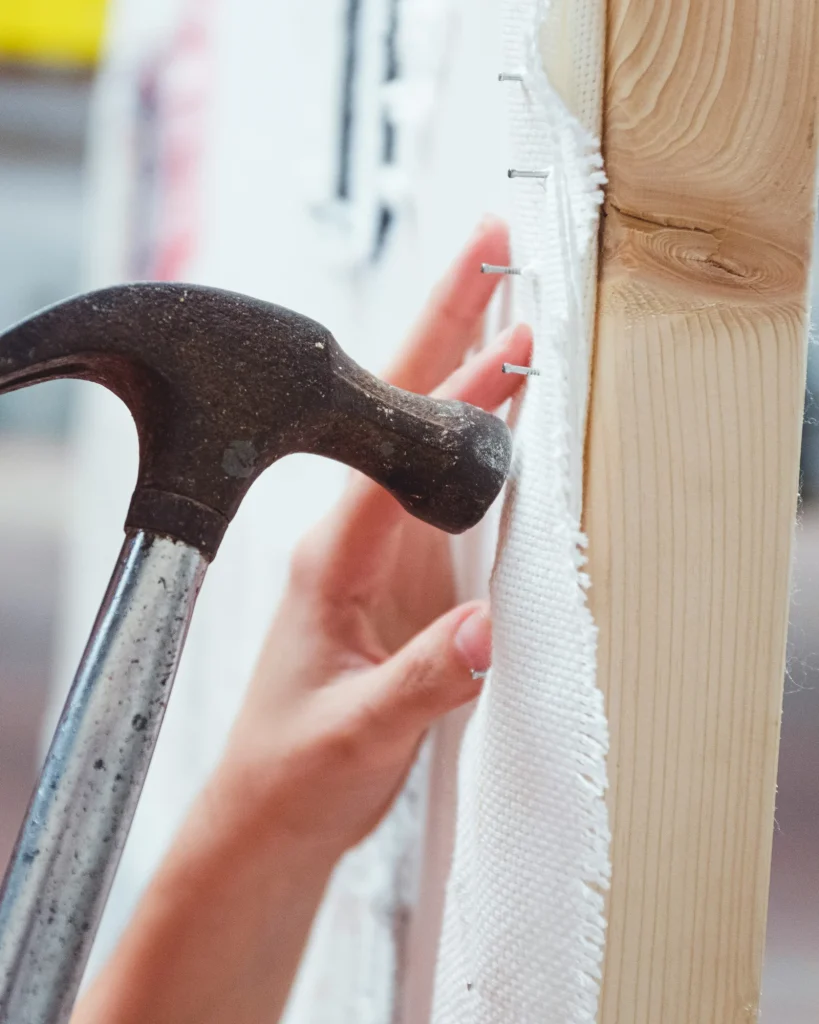 A hammer securing upholstery fabric along a timber frame.