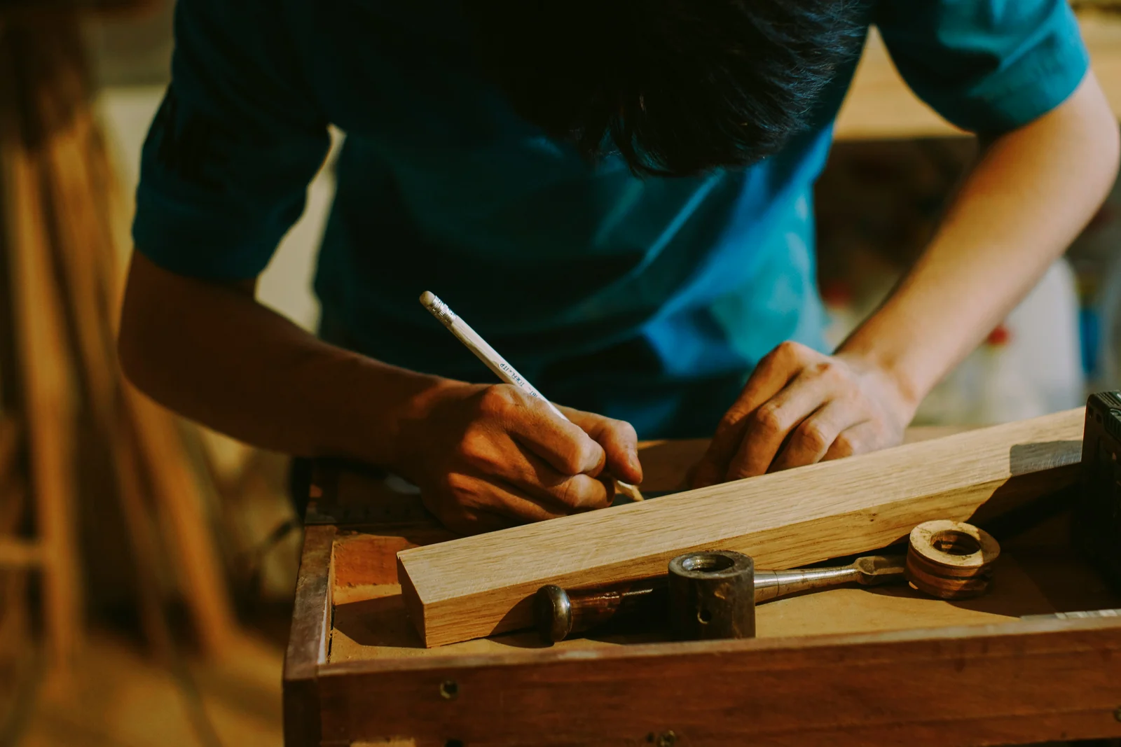 A craftsperson marking a measurement on a timber piece at a workbench.